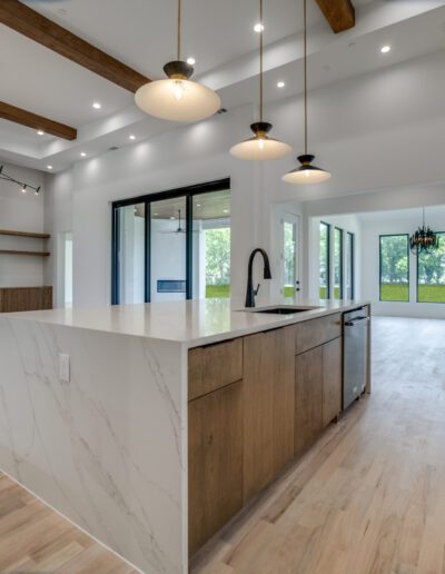 Modern kitchen interior with a marble island, wooden accents, and pendant lighting.