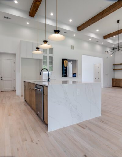 Modern spacious kitchen with white cabinetry, marble accents, and wooden beams.