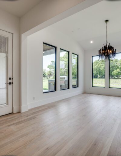A modern, empty room with large windows, hardwood floors, and a contemporary chandelier.