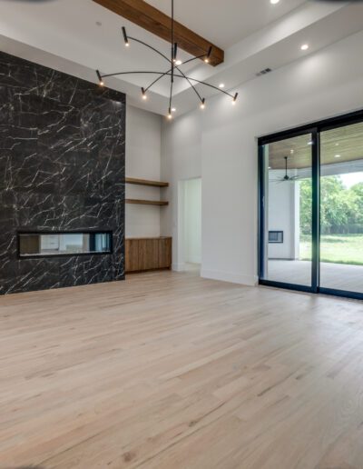 Modern living room with wooden floors, a black marble fireplace, built-in shelves, and large sliding glass doors leading to the outdoor area.