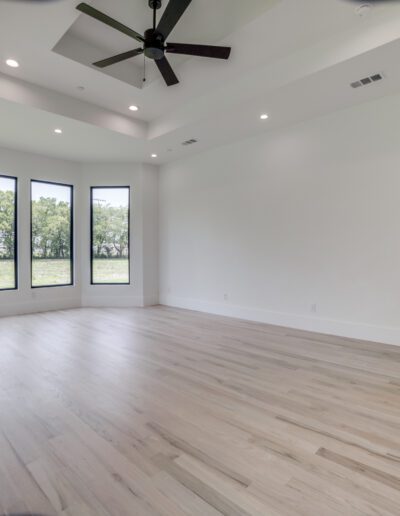 Spacious, empty room with hardwood flooring, tall windows, and a ceiling fan.