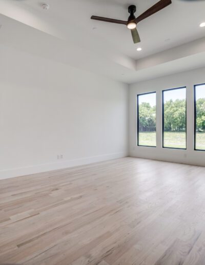 Empty modern living space with hardwood floors and large windows overlooking a green area.