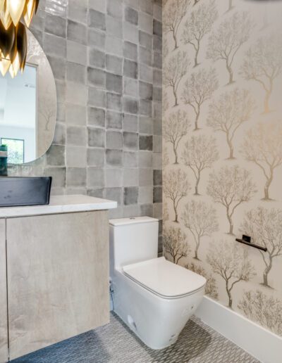 Modern bathroom with a wall-mounted toilet, tree-patterned wallpaper, and a vanity with a vessel sink.
