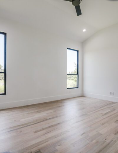 Bright, empty room with hardwood floors, two windows, and an open door.