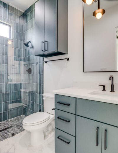 Modern bathroom interior with gray tile walls, glass-enclosed shower, and blue vanity cabinet.