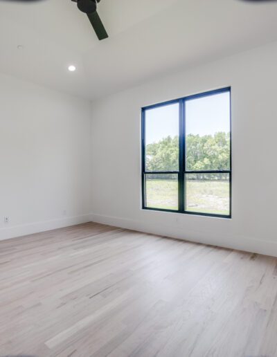 A bright, empty room with pale wooden floors and a large window with a view of greenery outside.