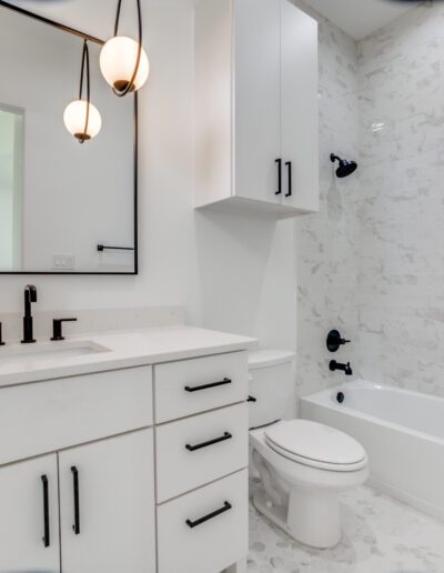 Modern bathroom interior with white cabinetry, marble tiling, and black fixtures.