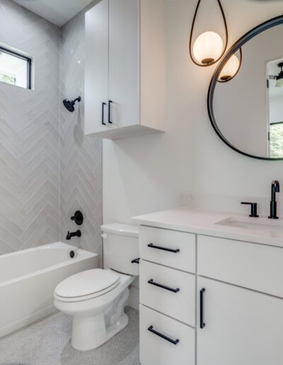 Modern bathroom featuring a herringbone tile pattern, white cabinetry, and sleek black fixtures.