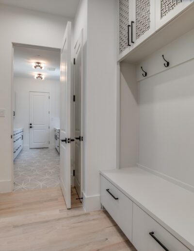 A bright, modern mudroom with a built-in bench, coat hooks, and a view into a kitchen with white cabinets.