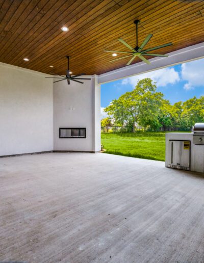 Spacious covered patio with a built-in grill and a view of a green lawn.