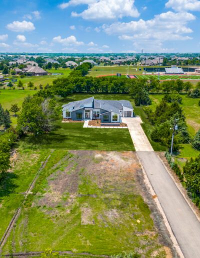 Aerial view of a single-story house with a large yard and surrounding open land under a blue sky with clouds.