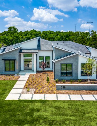 Modern single-story home with large windows and a spacious driveway, surrounded by a well-manicured lawn.