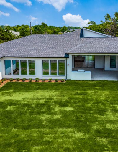 Aerial view of a single-story white house with a gray roof and large windows, surrounded by a well-manicured lawn.