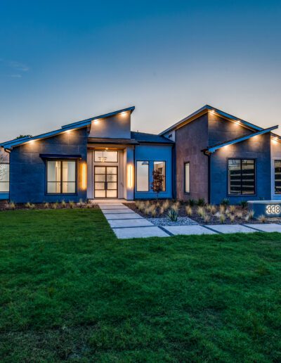 Modern single-story home with a flat roof and large windows, set against a twilight sky.
