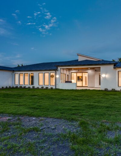 Modern single-story house illuminated at twilight with a large lawn in the foreground.