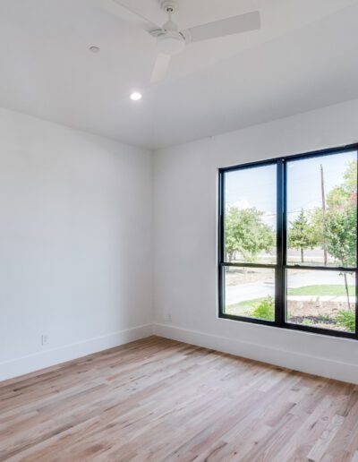 Bright, empty room with hardwood floors and a large window with a view of the outdoors.