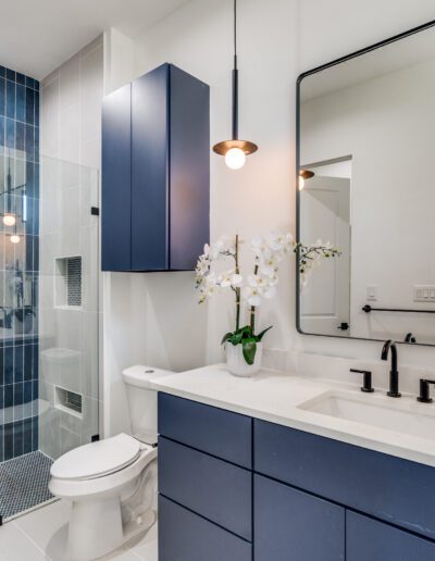 Modern bathroom with blue vanity, walk-in shower, and wall-mounted toilet.