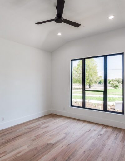 Empty room with hardwood floors, a large window, and a ceiling fan.