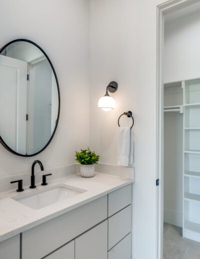 Modern bathroom interior with a white vanity, round mirror, and wall-mounted lights.