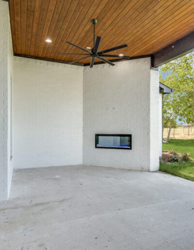Spacious covered patio with a ceiling fan and a built-in fireplace, overlooking a green lawn.