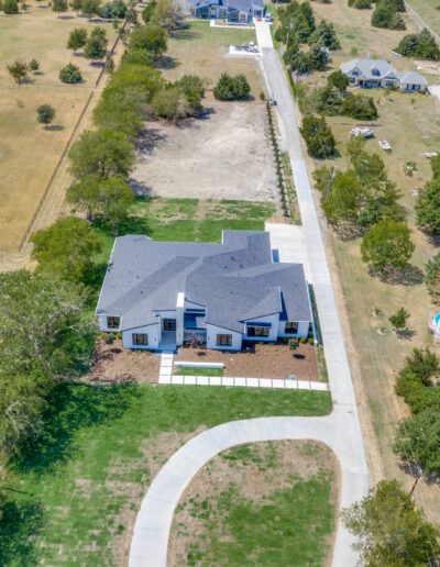 Aerial view of a suburban house with a curved driveway and sparsely vegetated surroundings.