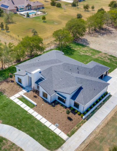 Aerial view of a modern single-story house with a gray roof, surrounded by a freshly landscaped yard and adjacent to open land.