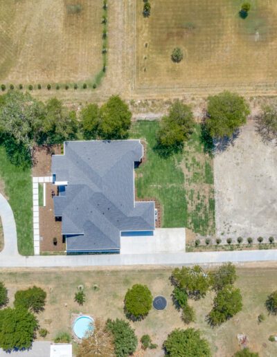 Aerial view of a suburban home with a curved driveway surrounded by green lawns and trees.
